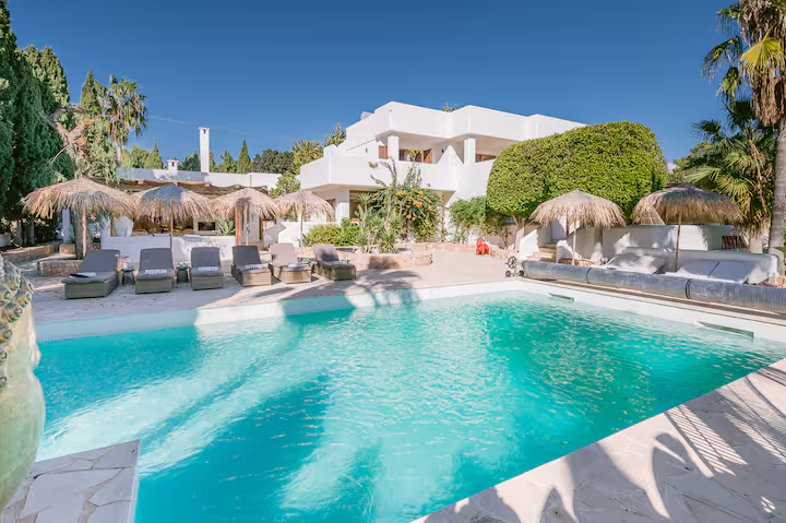 White Ibiza villa beside a turquoise pool and thatched parasols